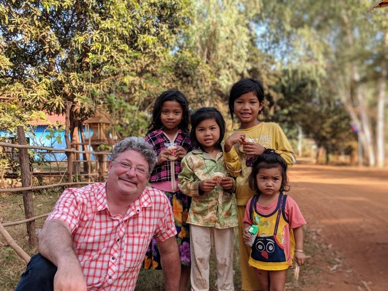 Professor Benjamin Bostick under a mango tree with a group of children outside a local rice farmer’s home. Photo: Ben Bostick